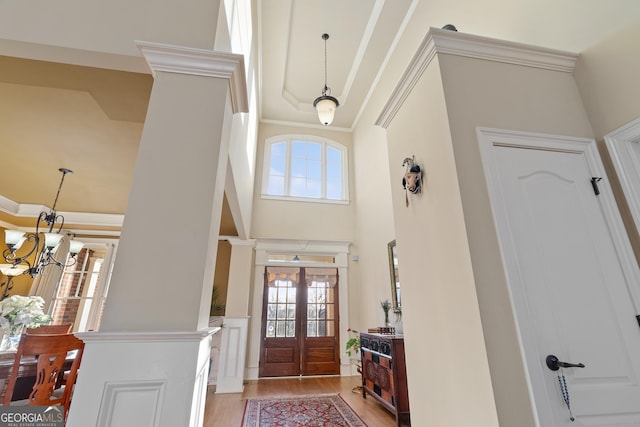 entryway with light wood-style flooring, french doors, a notable chandelier, and ornamental molding