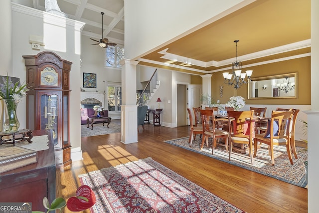 dining room featuring a towering ceiling, wood finished floors, crown molding, decorative columns, and ceiling fan with notable chandelier