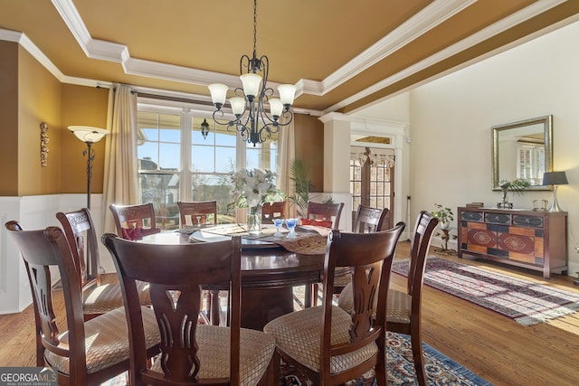 dining room featuring a raised ceiling, wood finished floors, a chandelier, and ornamental molding