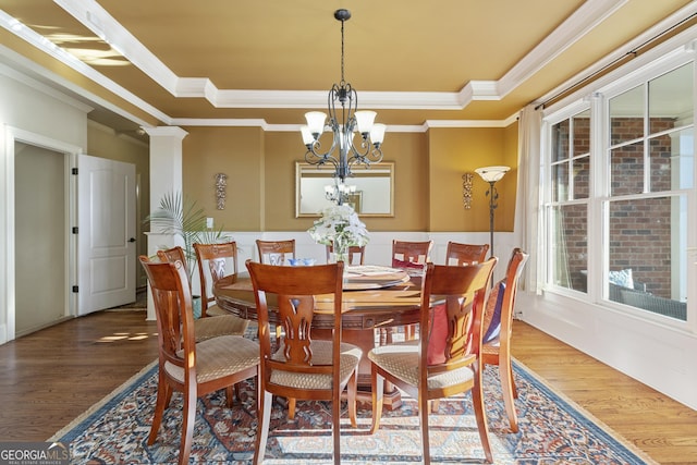 dining space with ornamental molding, a notable chandelier, a tray ceiling, and wood finished floors