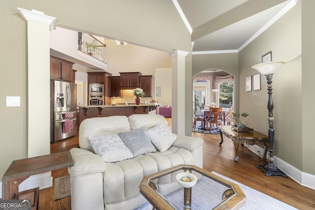 living area with arched walkways, light wood-style floors, crown molding, and baseboards