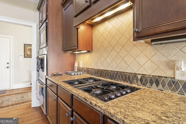 kitchen featuring black gas cooktop, backsplash, stainless steel microwave, light wood-style floors, and light stone countertops
