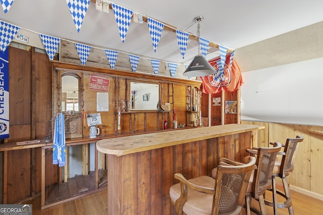 bar with wood finished floors, a bar, and wood walls