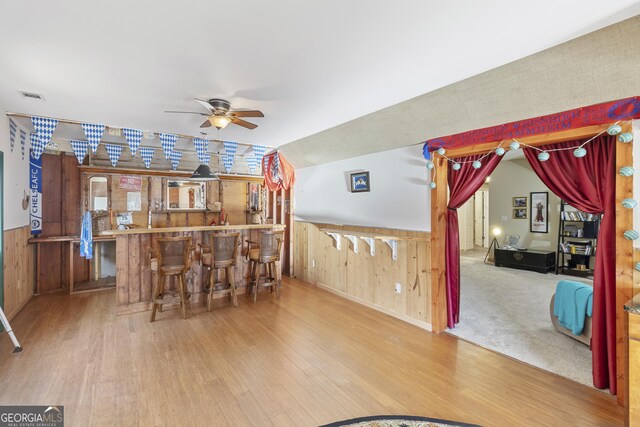 bar featuring wood walls, wood finished floors, visible vents, a ceiling fan, and a bar