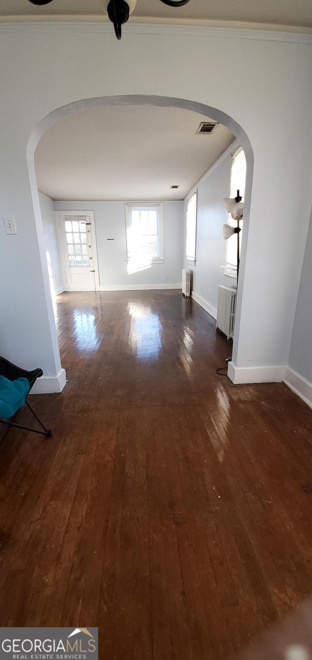 corridor featuring hardwood / wood-style flooring, radiator, arched walkways, and visible vents