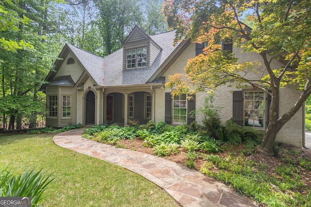 view of front of property featuring roof with shingles, stucco siding, and a front yard