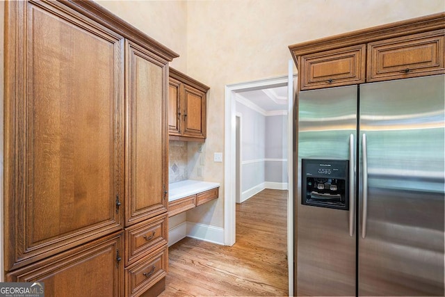 kitchen with light wood-style floors, brown cabinetry, crown molding, built in study area, and stainless steel fridge
