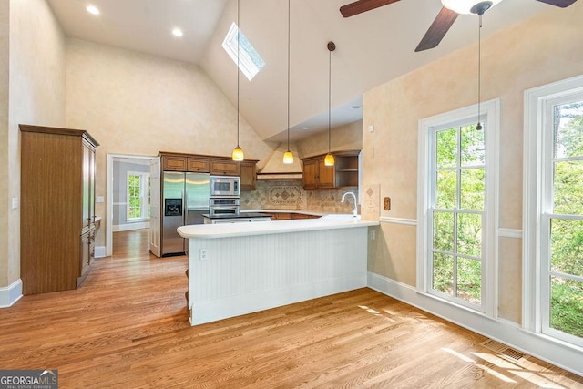 kitchen featuring a peninsula, high vaulted ceiling, appliances with stainless steel finishes, and light wood finished floors