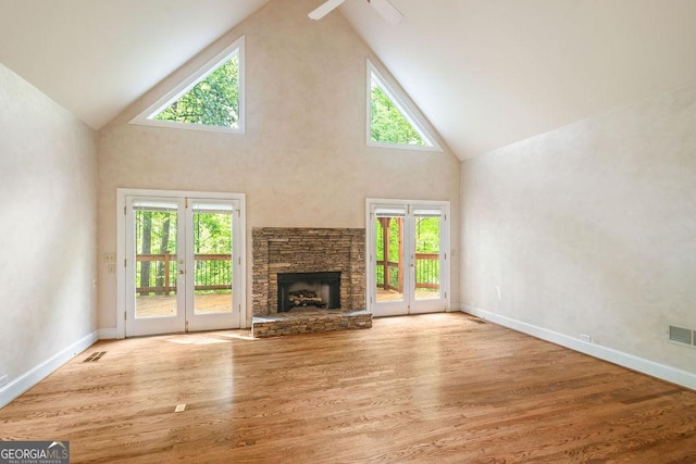 unfurnished living room with visible vents, a fireplace, wood finished floors, high vaulted ceiling, and baseboards