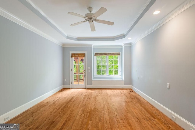 unfurnished room featuring a ceiling fan, crown molding, baseboards, light wood finished floors, and a tray ceiling