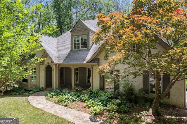view of front of property featuring a porch, a front lawn, roof with shingles, and stucco siding
