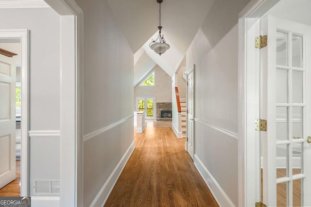 hall featuring baseboards, vaulted ceiling, wood finished floors, and visible vents