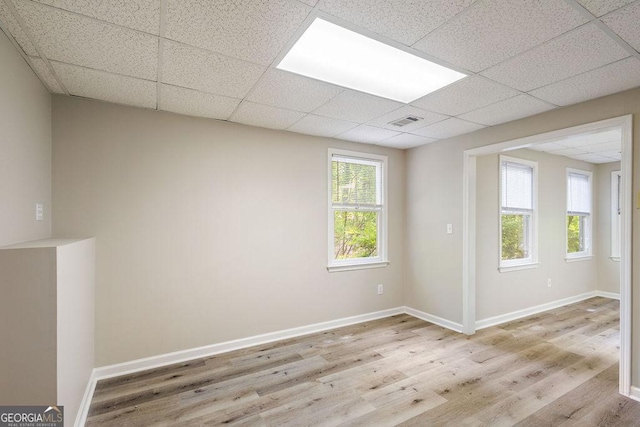 spare room featuring baseboards, a drop ceiling, wood finished floors, and visible vents