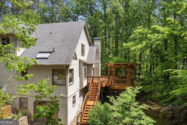 view of home's exterior featuring a chimney, a deck, stairway, a shingled roof, and stucco siding
