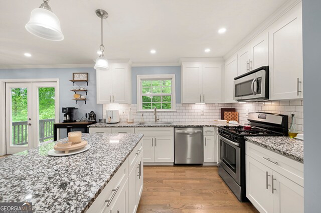 kitchen featuring appliances with stainless steel finishes, a sink, white cabinets, light wood-style floors, and crown molding