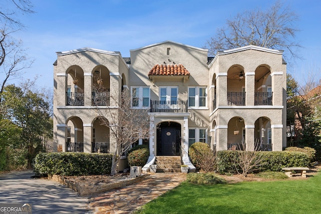 mediterranean / spanish house featuring a tile roof, a front lawn, a balcony, and stucco siding