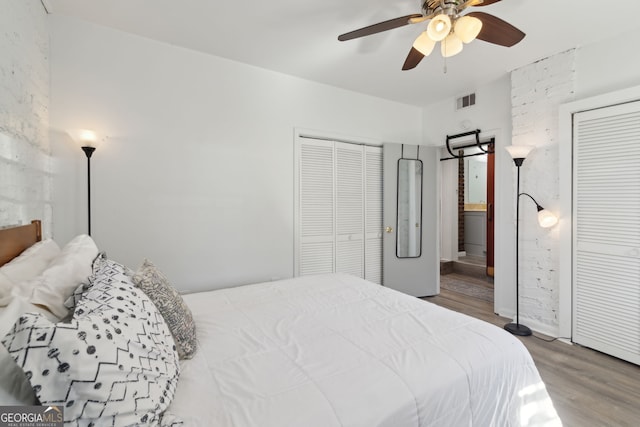bedroom featuring visible vents, a ceiling fan, wood finished floors, multiple closets, and connected bathroom