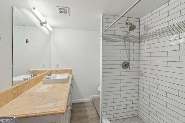 full bathroom with toilet, a tile shower, visible vents, wood finished floors, and vanity
