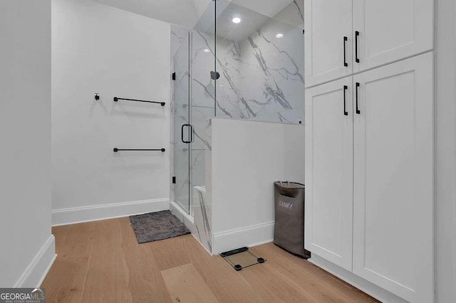 bathroom featuring baseboards, wood finished floors, a marble finish shower, and recessed lighting
