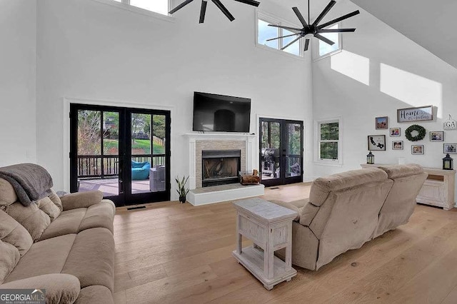 living area featuring a ceiling fan, french doors, a towering ceiling, and light wood-type flooring