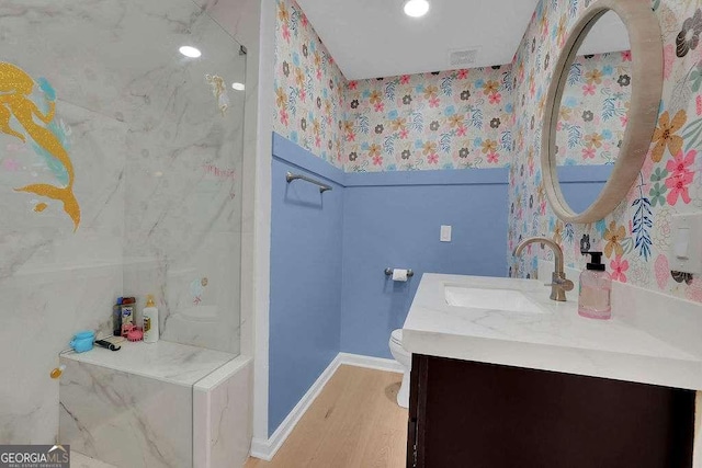 bathroom featuring wallpapered walls, wood finished floors, toilet, vanity, and baseboards