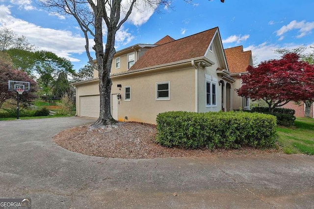 view of side of property with a garage, driveway, and stucco siding
