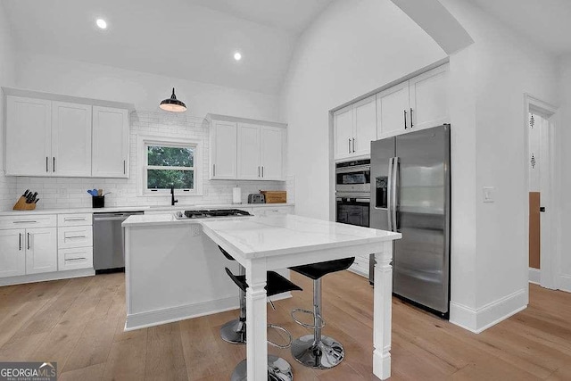 kitchen with decorative backsplash, light wood-type flooring, white cabinetry, a kitchen bar, and appliances with stainless steel finishes
