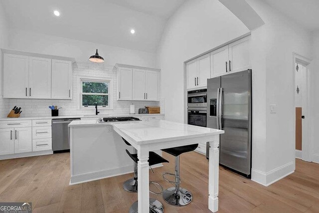 3060 Cabernet Ct, Cumming, GA 30041 - kitchen featuring stainless steel appliances, a kitchen bar, white cabinets, tasteful backsplash, and light wood finished floors