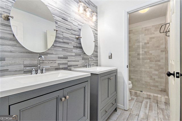 4440 Spring Mtn Ln, Powder Springs, GA 30127 - bathroom featuring two vanities, backsplash, a tile shower, and wood finished floors