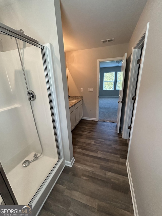 bathroom with wood finished floors, a shower stall, baseboards, and vanity