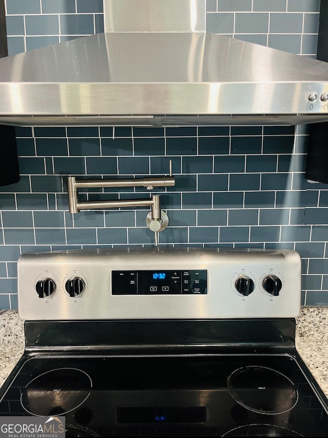 kitchen view of stainless steel electric stove, decorative backsplash, and light stone counters