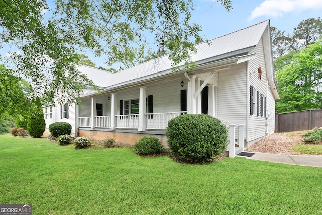 view of front of home with a porch, a front lawn, metal roof, and fence