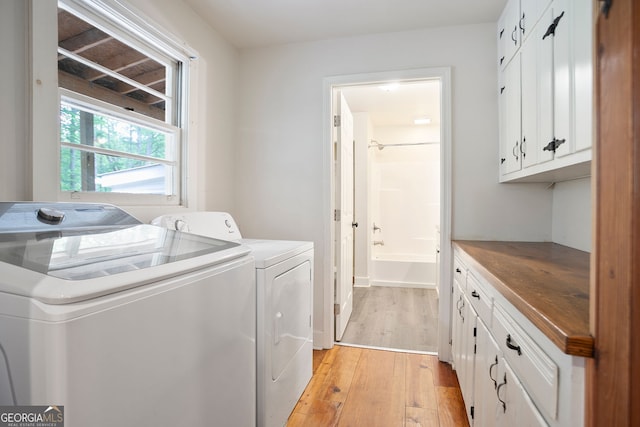 clothes washing area featuring separate washer and dryer, cabinet space, and light wood-style floors