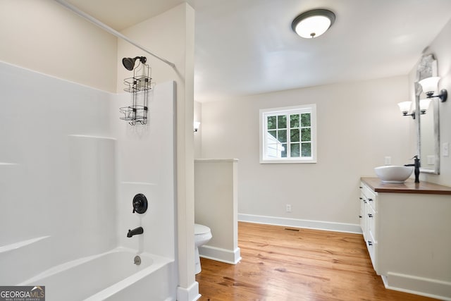 bathroom featuring wood finished floors, toilet, shower / tub combination, vanity, and baseboards