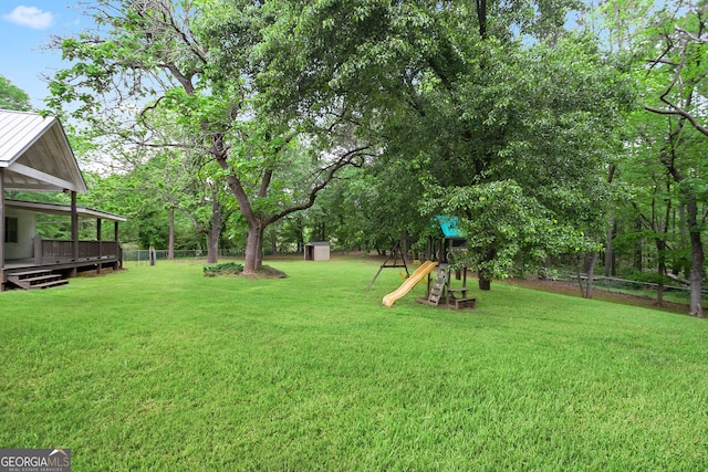 view of yard featuring an outdoor structure, a storage unit, fence, a wooden deck, and a playground