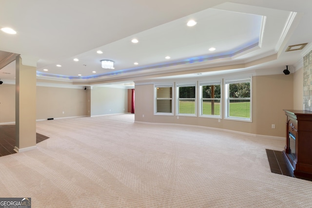 unfurnished living room with light carpet, crown molding, a tray ceiling, and baseboards