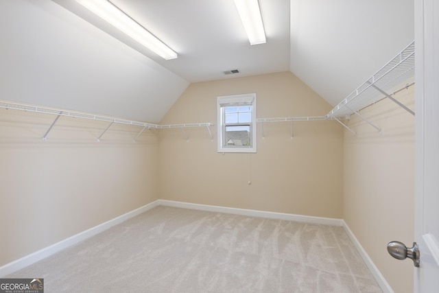 spacious closet featuring light carpet, vaulted ceiling, and visible vents