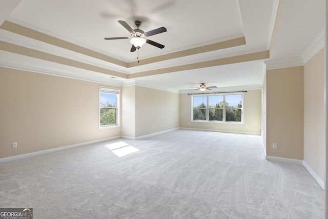 empty room featuring a ceiling fan, crown molding, light carpet, a tray ceiling, and baseboards