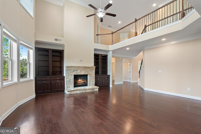 unfurnished living room with a towering ceiling, wood finished floors, baseboards, a fireplace, and ceiling fan