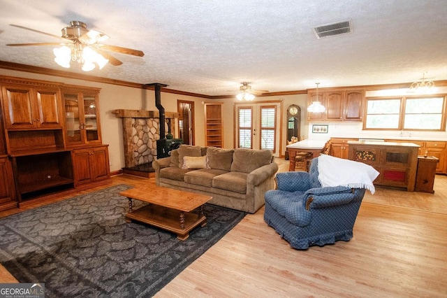 living area with a wood stove, visible vents, ornamental molding, light wood-style flooring, and ceiling fan