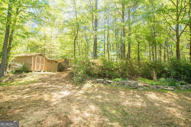 view of yard with an outdoor structure, a view of trees, and a shed