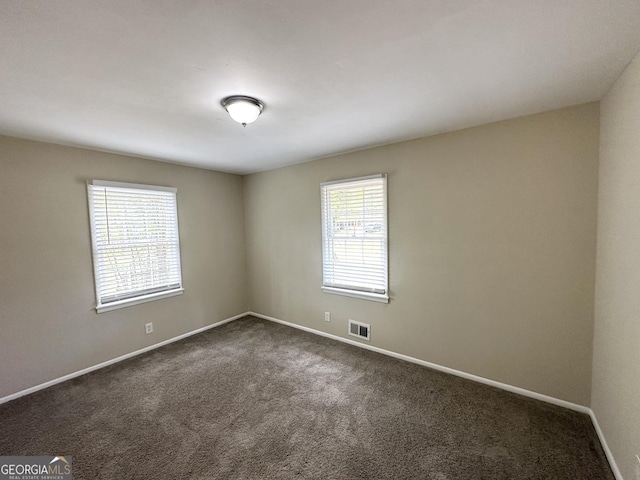 spare room featuring dark colored carpet, visible vents, and baseboards
