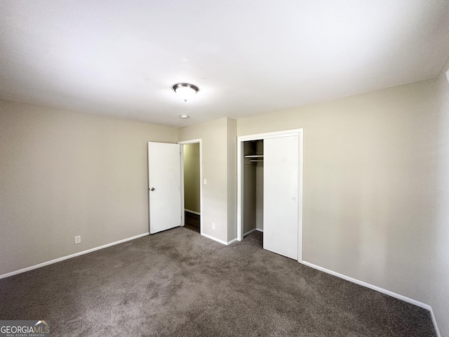 unfurnished bedroom featuring baseboards, dark carpet, and a closet