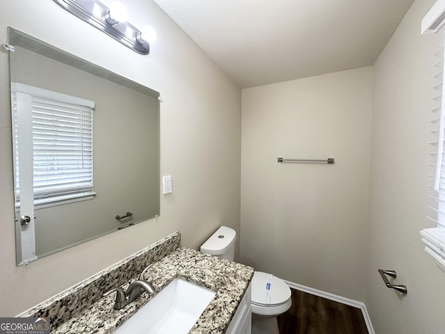 half bath with toilet, vanity, wood finished floors, and a wealth of natural light