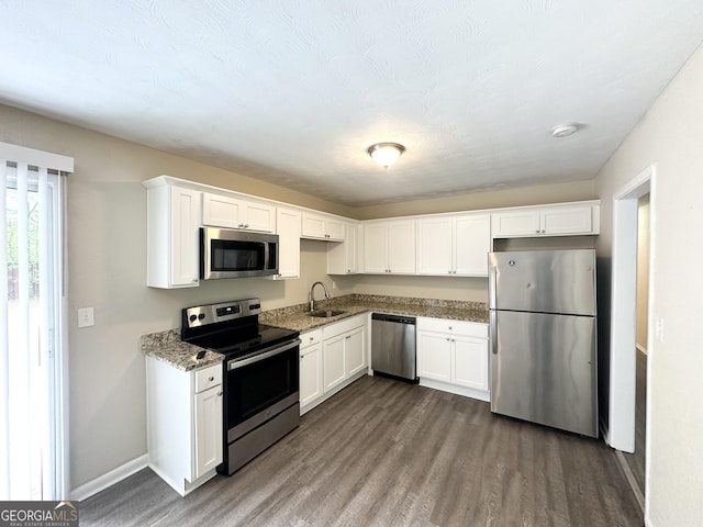 kitchen featuring stainless steel appliances, dark wood-style floors, a sink, white cabinetry, and light stone counters