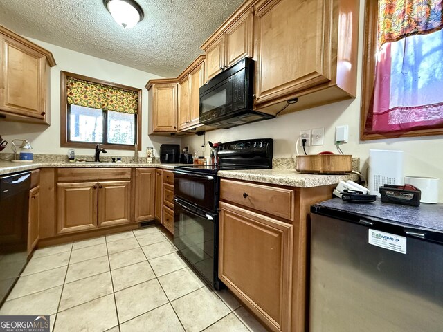 kitchen with brown cabinets, a sink, a textured ceiling, light tile patterned floors, and black appliances