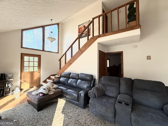 living room featuring wood finished floors, stairs, a textured ceiling, and a towering ceiling