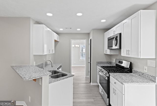 kitchen featuring a peninsula, a sink, baseboards, light stone countertops, and appliances with stainless steel finishes
