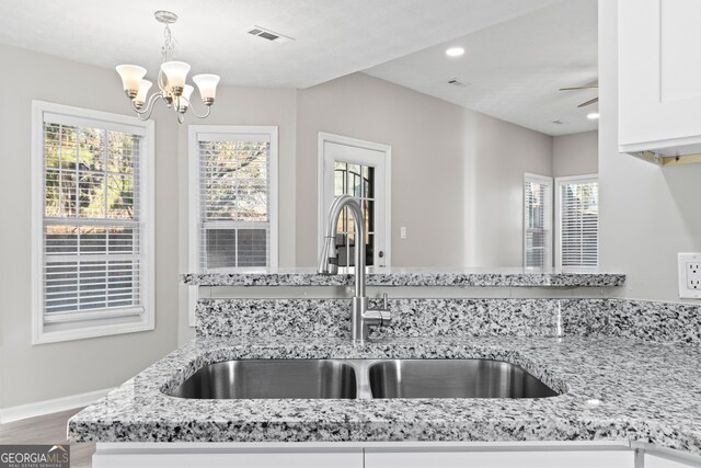 kitchen with visible vents, a sink, white cabinetry, and light stone counters
