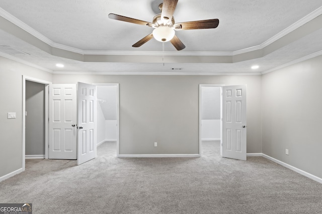 unfurnished bedroom featuring a tray ceiling, carpet flooring, ornamental molding, and a walk in closet